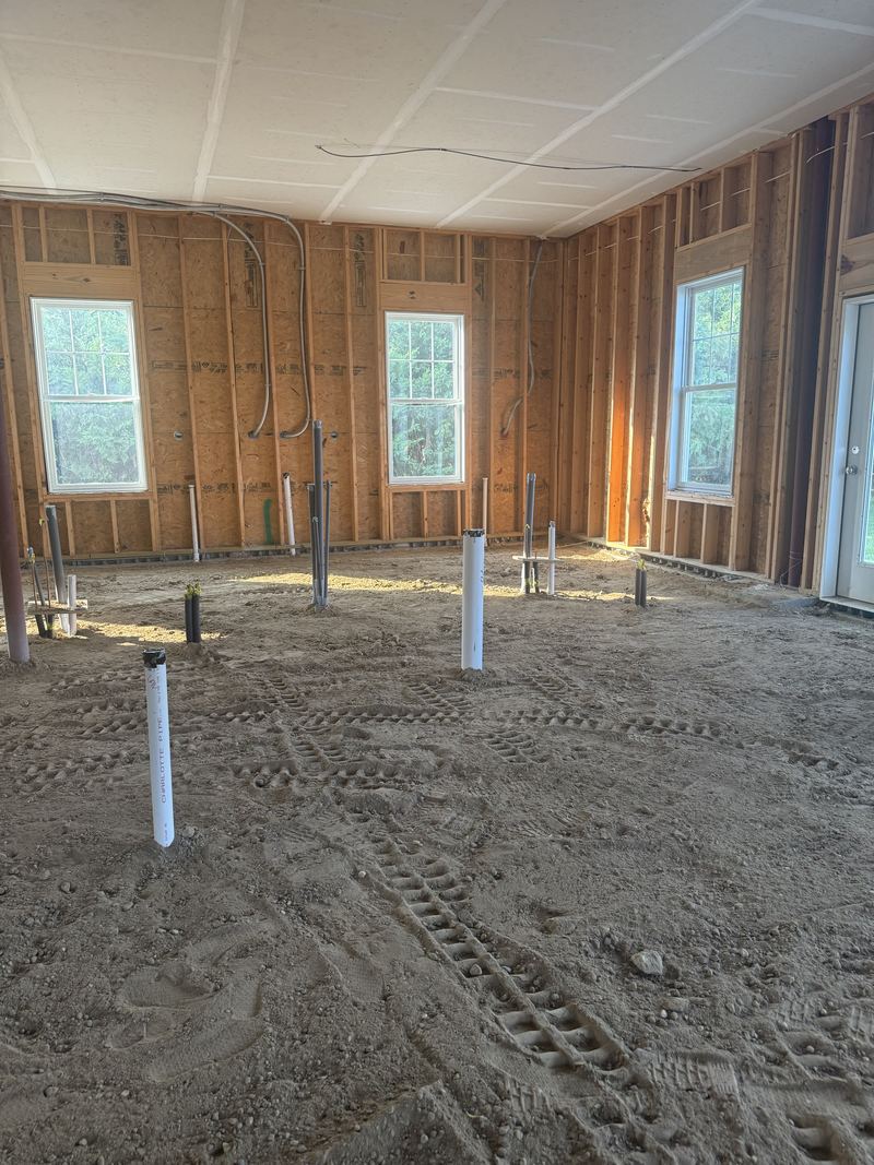 Compacted dirt floor showing roller tracks, with capped plumbing stub-ups spaced across it.