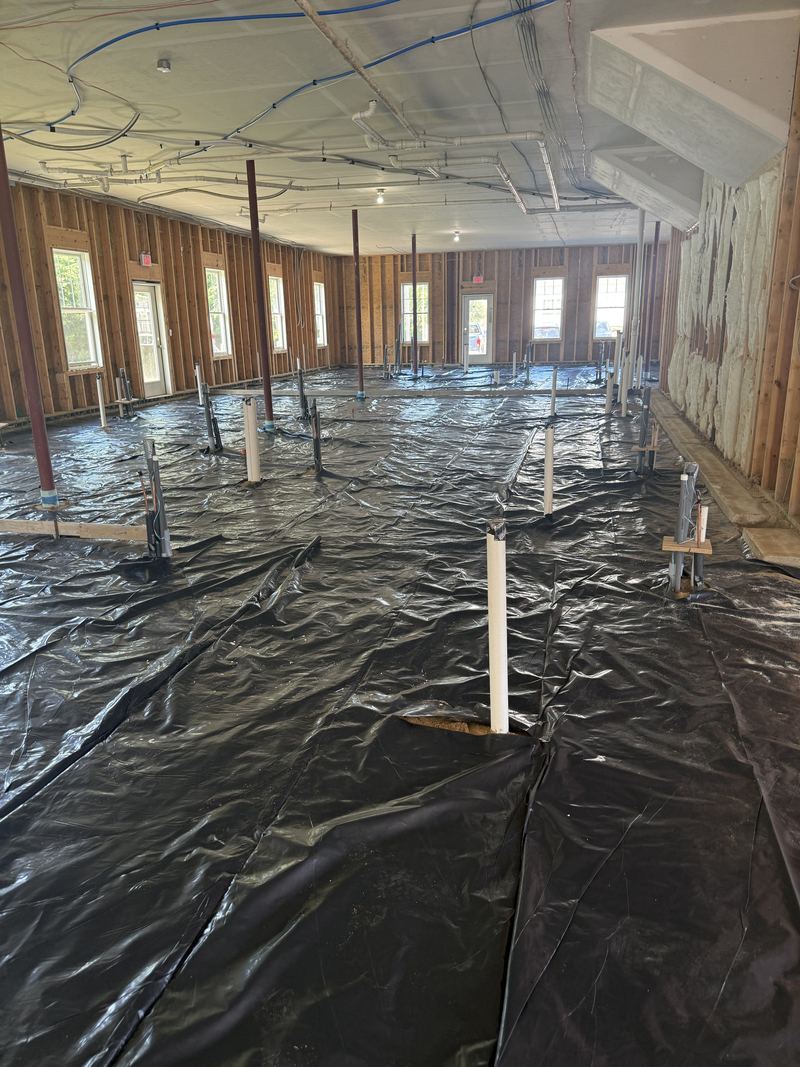 Black vapor barrier laid across the full floor with plumbing stub-ups sleeved through it, ready for concrete.